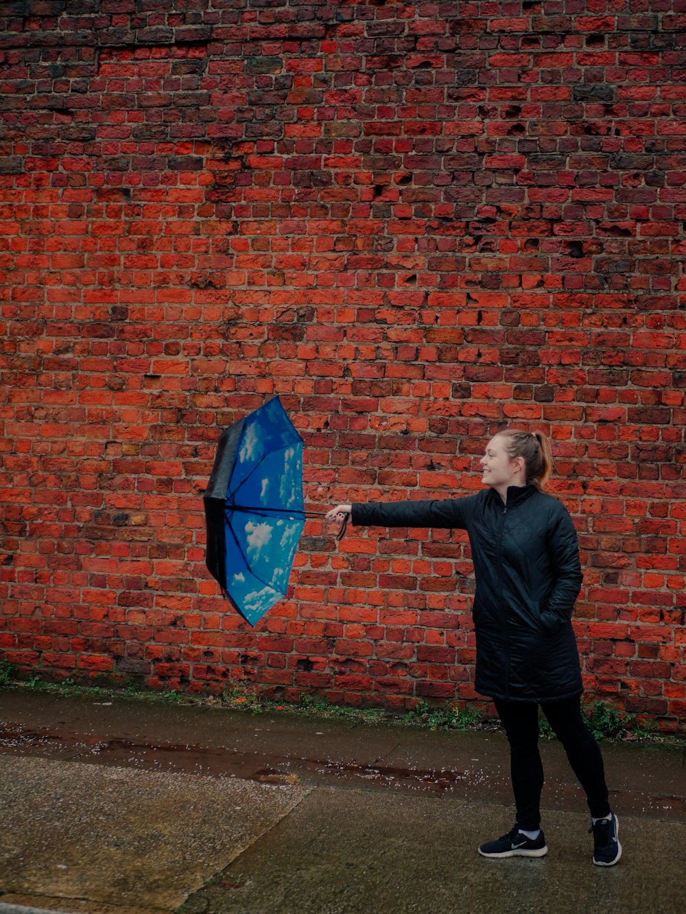 a woman holding a blue umbrella in front of a brick wall