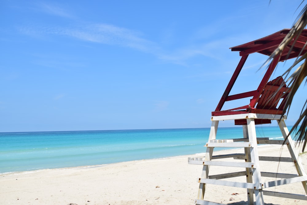 a red chair sitting on top of a beach next to the ocean