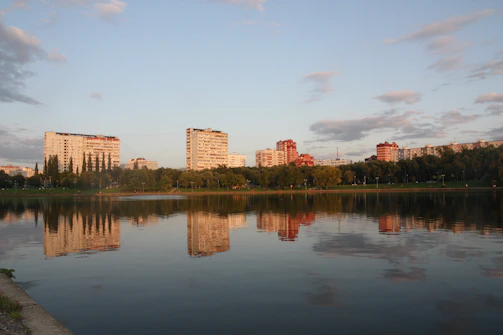 A panoramic view of a luxury apartment complex nestled near a serene lake, with balconies overlooking the water.