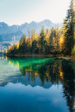 A quiet mountain lake reflecting the vibrant colors of autumn leaves at dusk.
