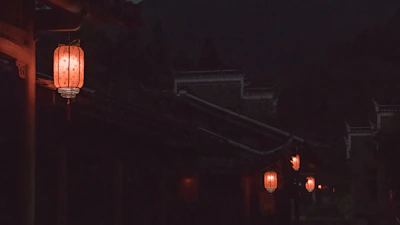 A traditional Malay village scene at dusk, with lanterns glowing softly.