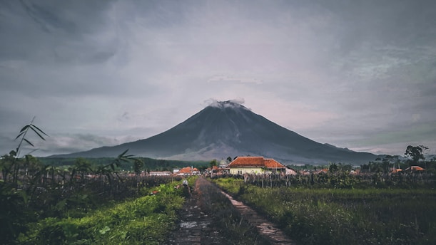 a dirt road in front of a mountain under a cloudy sky