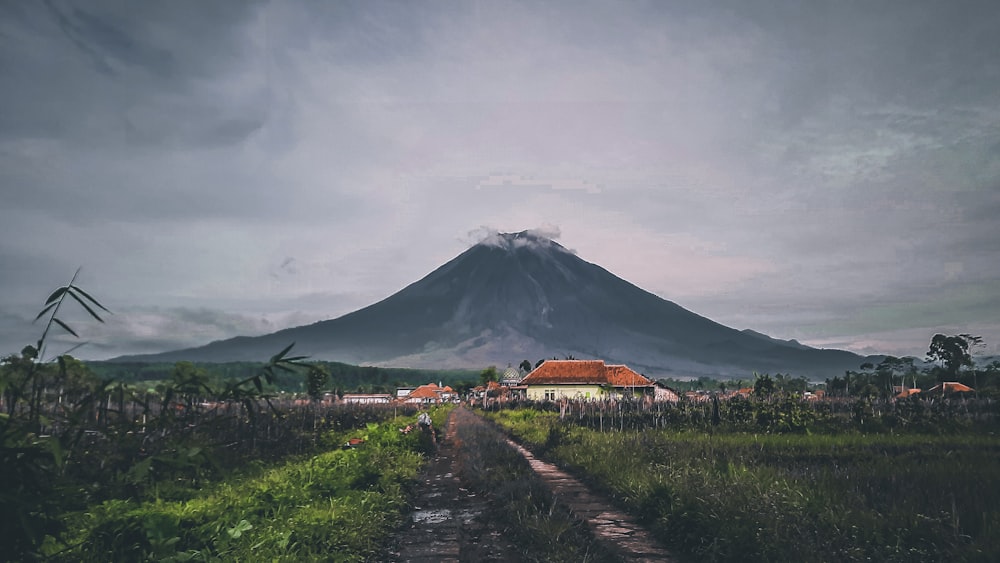 a dirt road in front of a mountain under a cloudy sky