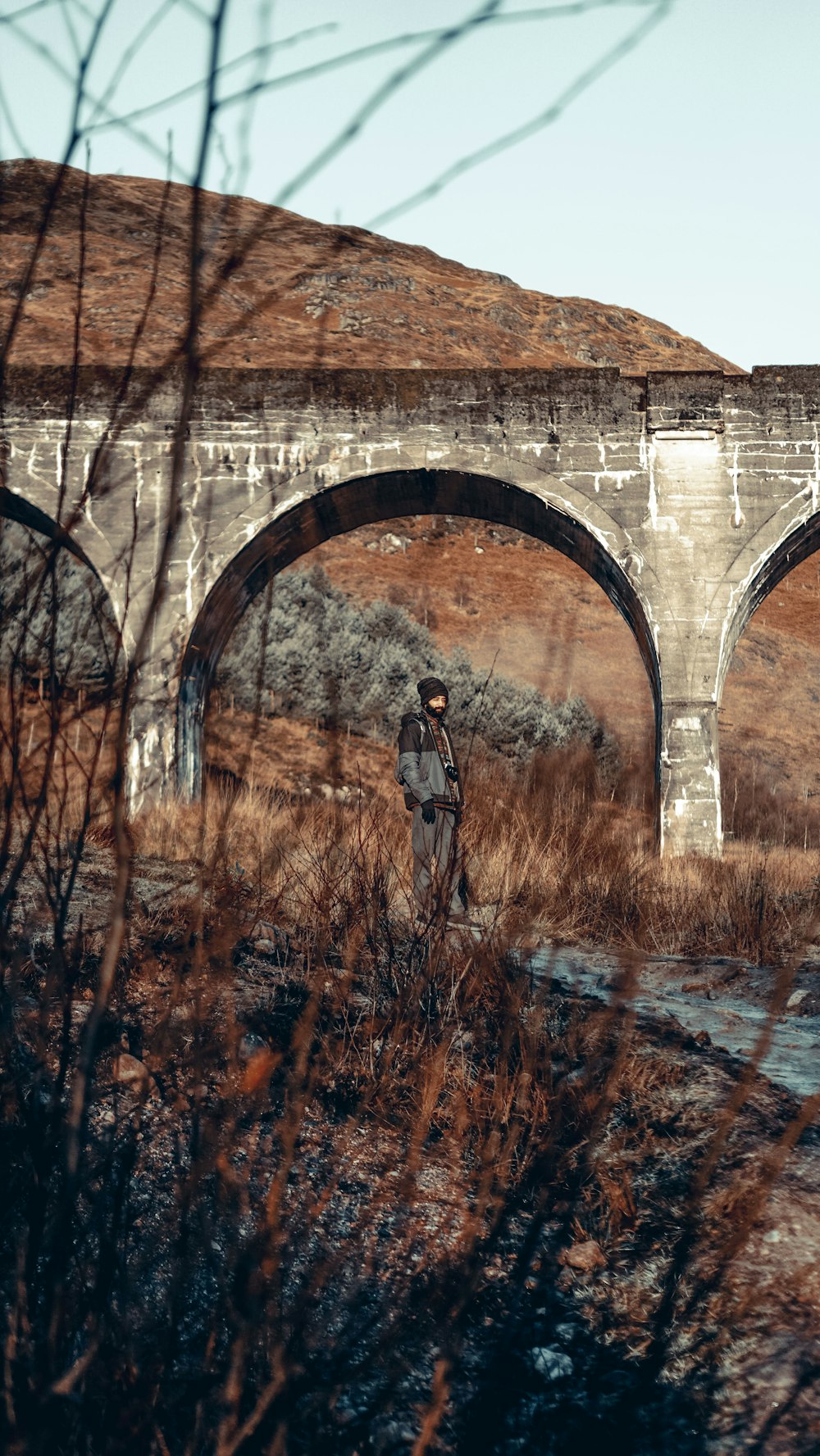 a man standing in front of a stone bridge