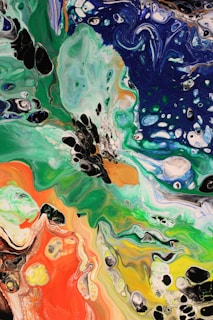 An abstract painting with flowing patterns and vibrant colors, including shades of green, blue, orange, red, and black. The paint appears to be swirled, creating a marbled effect with various shapes and textures.