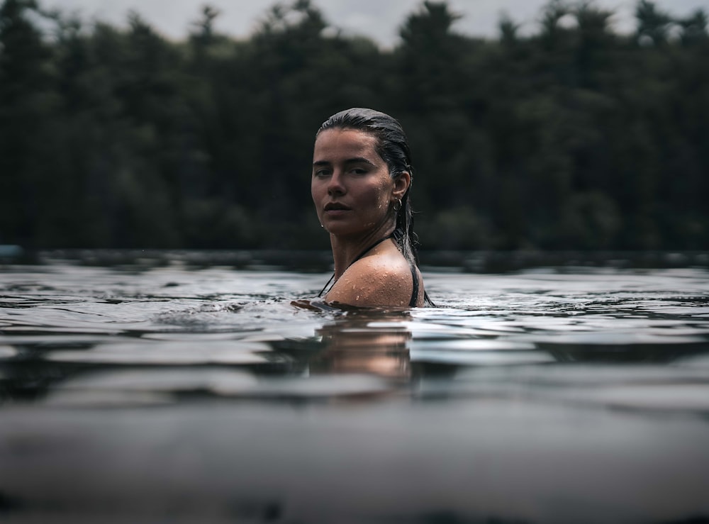 a woman swimming in a lake with trees in the background