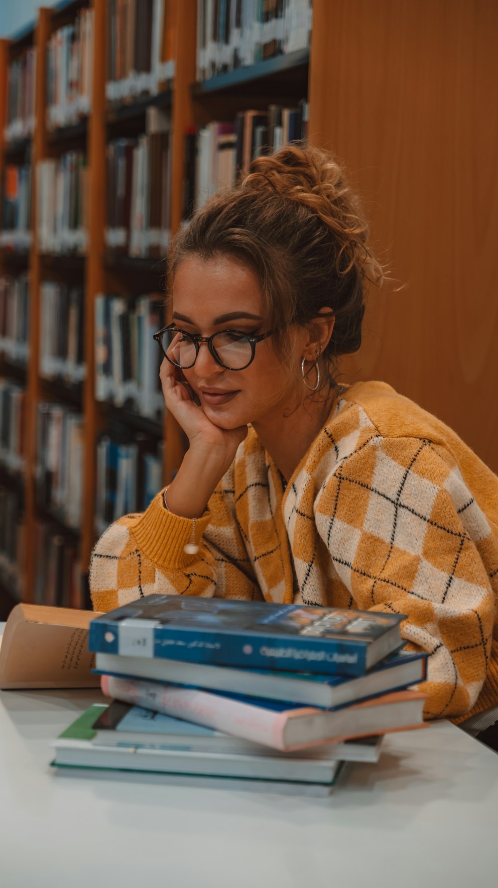 a woman sitting at a table in front of a stack of books