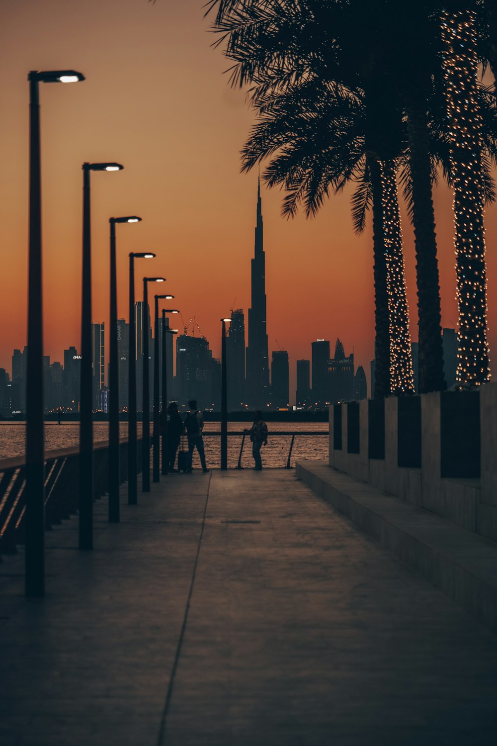 a couple of people walking down a sidewalk next to palm trees