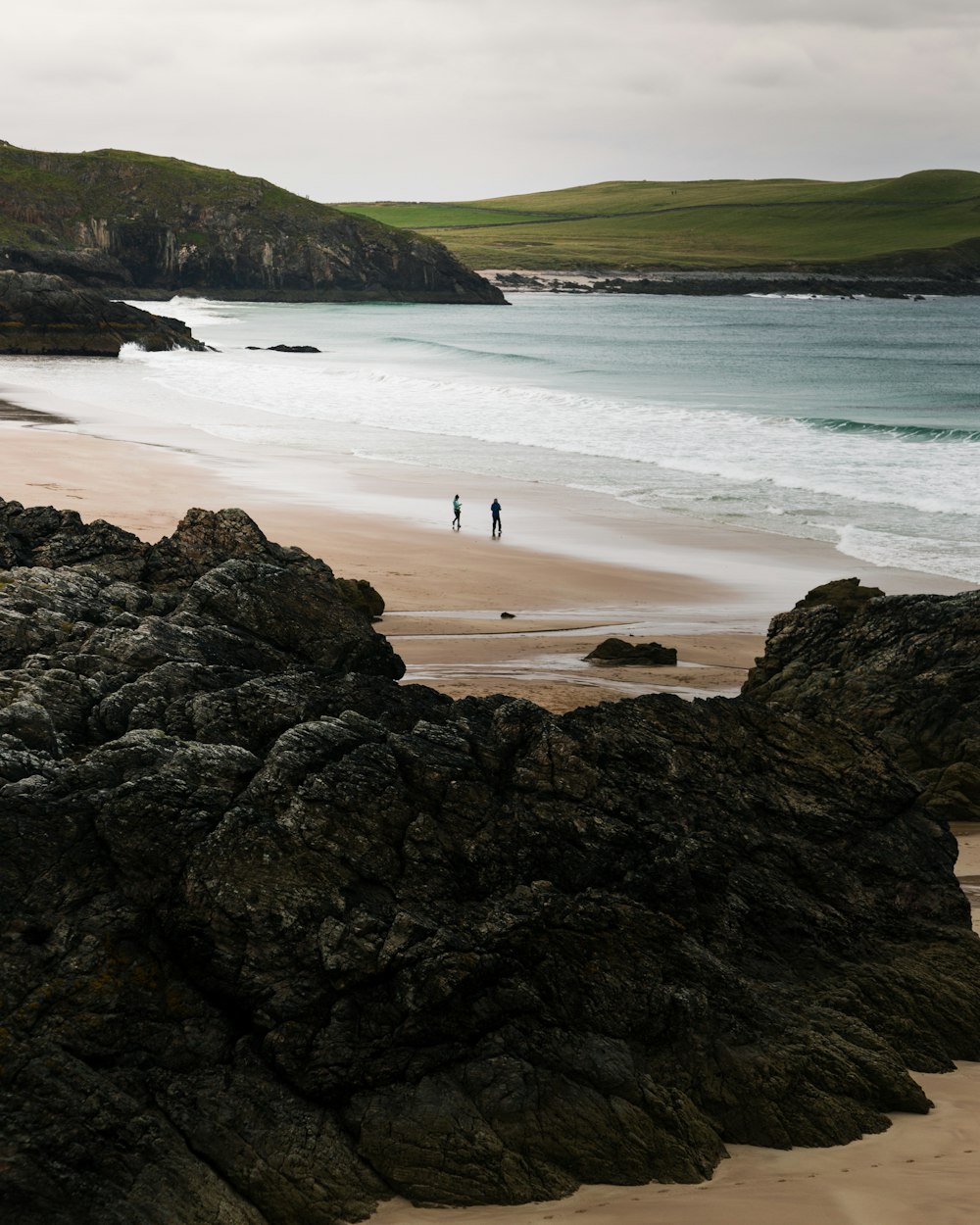 two people walking on a beach next to the ocean