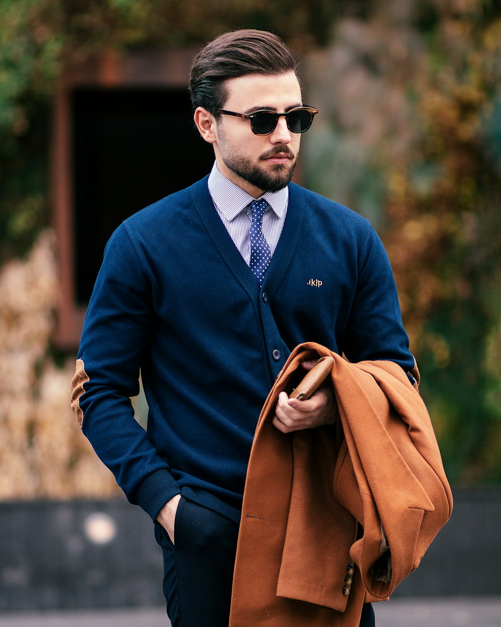 Un uomo in un maglione blu e cravatta che porta una borsa marrone