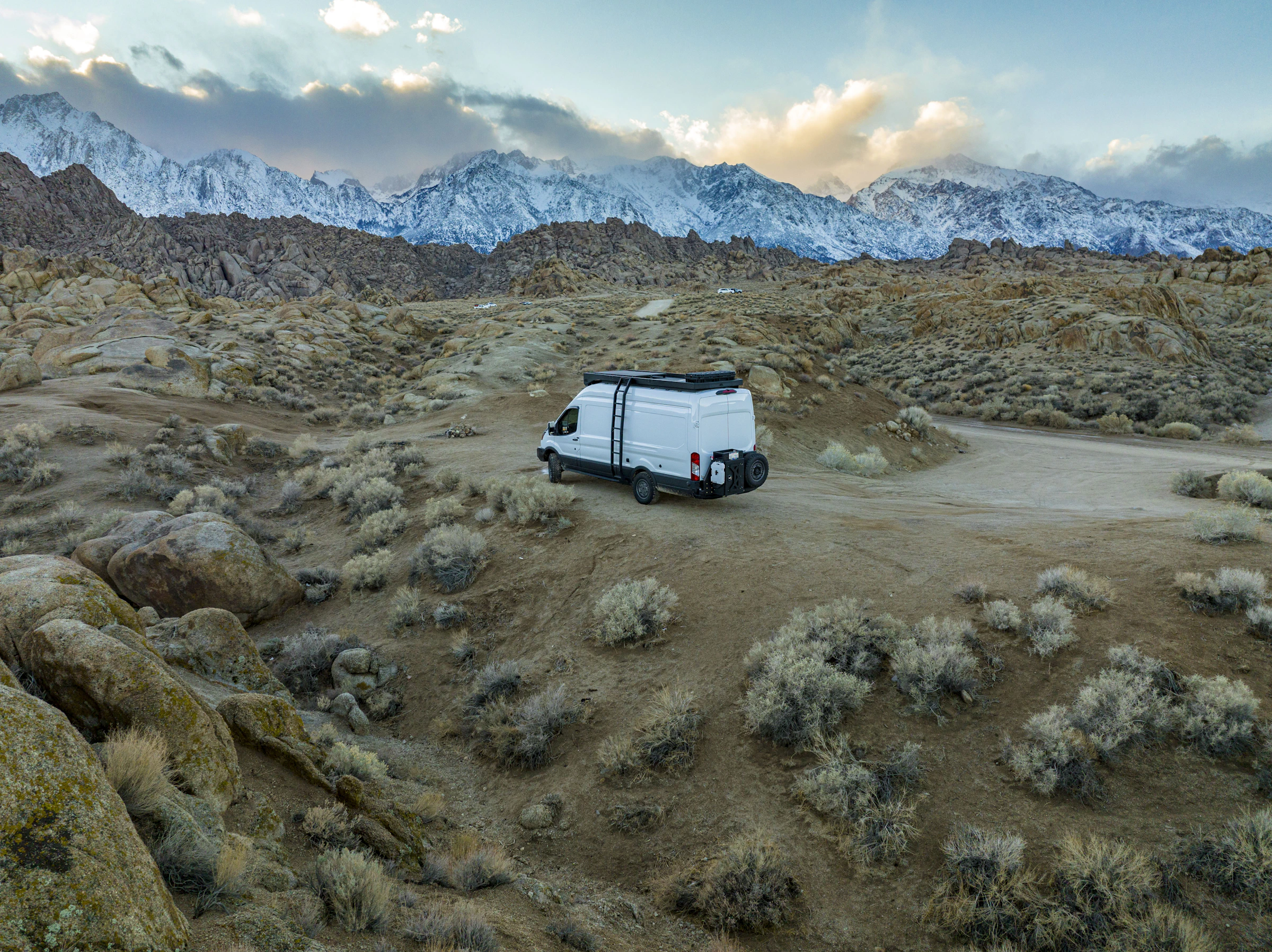 A camper van in an open rocky desert below snow-covered mountains
