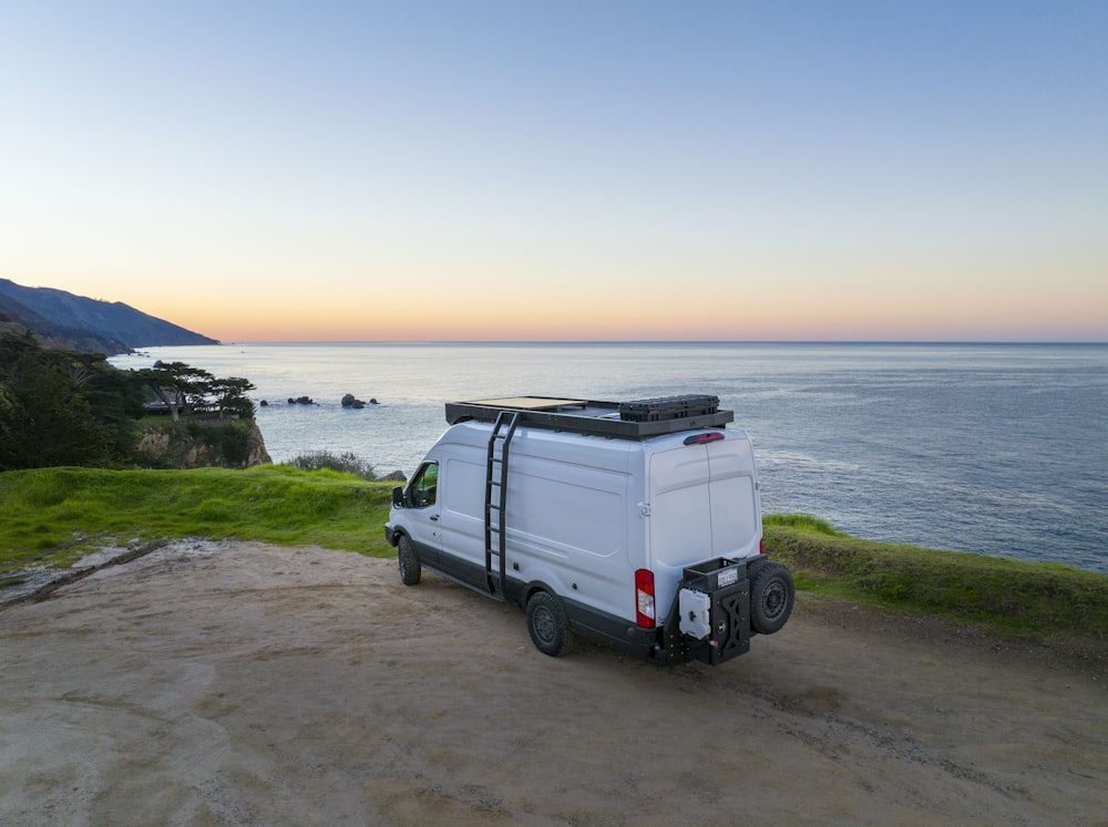 a white van parked on top of a dirt road next to the ocean