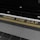 The image features a train platform edge with the phrase 'MIND THE GAP' written in yellow on a black strip. The phrase is aligned above a yellow line that separates the platform from the tracks. The foreground includes tactile paving with raised dots, commonly used as a safety feature in train stations.