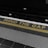 The image features a train platform edge with the phrase 'MIND THE GAP' written in yellow on a black strip. The phrase is aligned above a yellow line that separates the platform from the tracks. The foreground includes tactile paving with raised dots, commonly used as a safety feature in train stations.