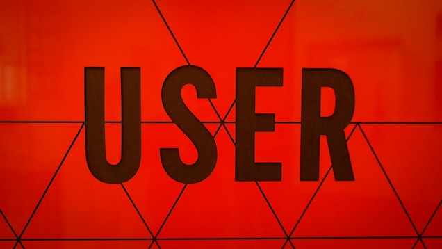 Bold, black typography spells the word 'USER' against a vibrant orange background with geometric triangular patterns.