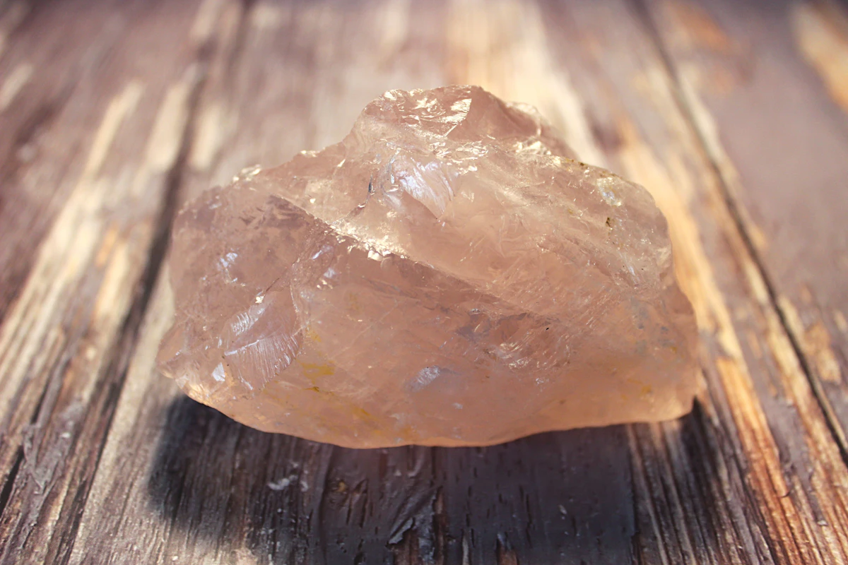 A polished rose-pink quartz piece on a wooden surface, the most-reached-for stone for heart-chakra work in contemporary practice