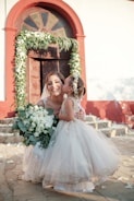 a little girl in a wedding dress holding a bouquet of flowers