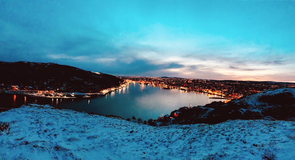 a lake surrounded by snow covered ground with a city in the distance