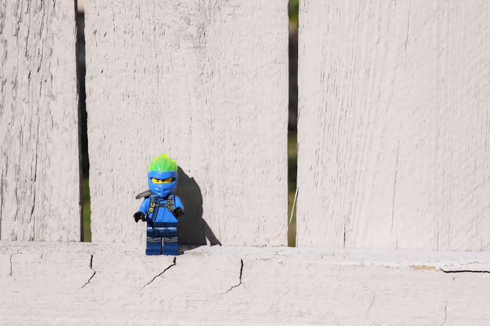 a lego man with green hair standing in front of a white wall