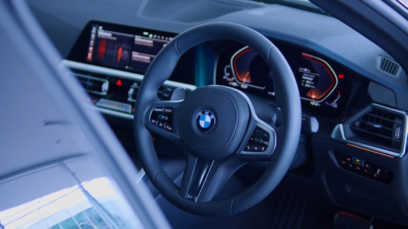 A car interior showcasing a sleek steering wheel with the BMW logo and advanced digital dashboard. The dashboard displays various controls and information with bright, colorful graphics. The interior design features a modern and technological aesthetic.