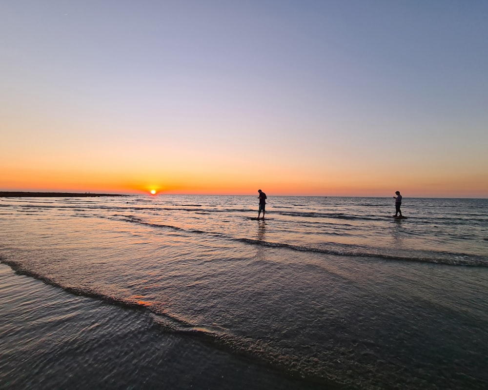 a couple of people standing on top of a beach near the ocean