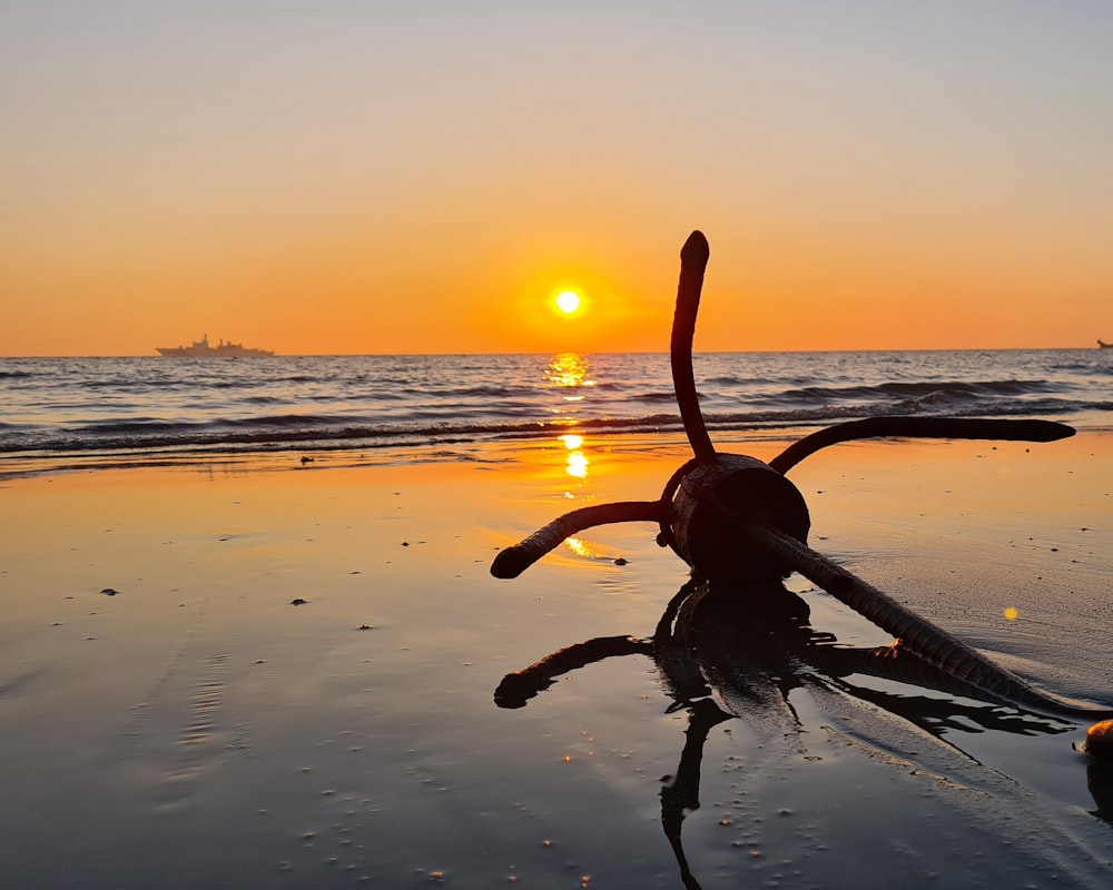 the sun is setting on a beach with a boat in the water