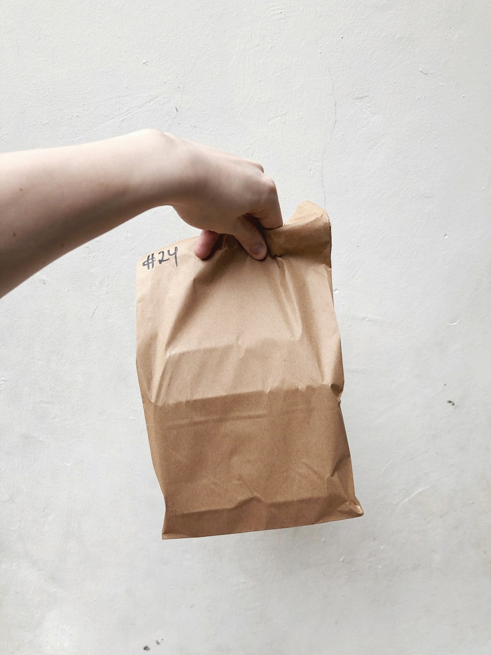 a person holding a brown paper bag with writing on it