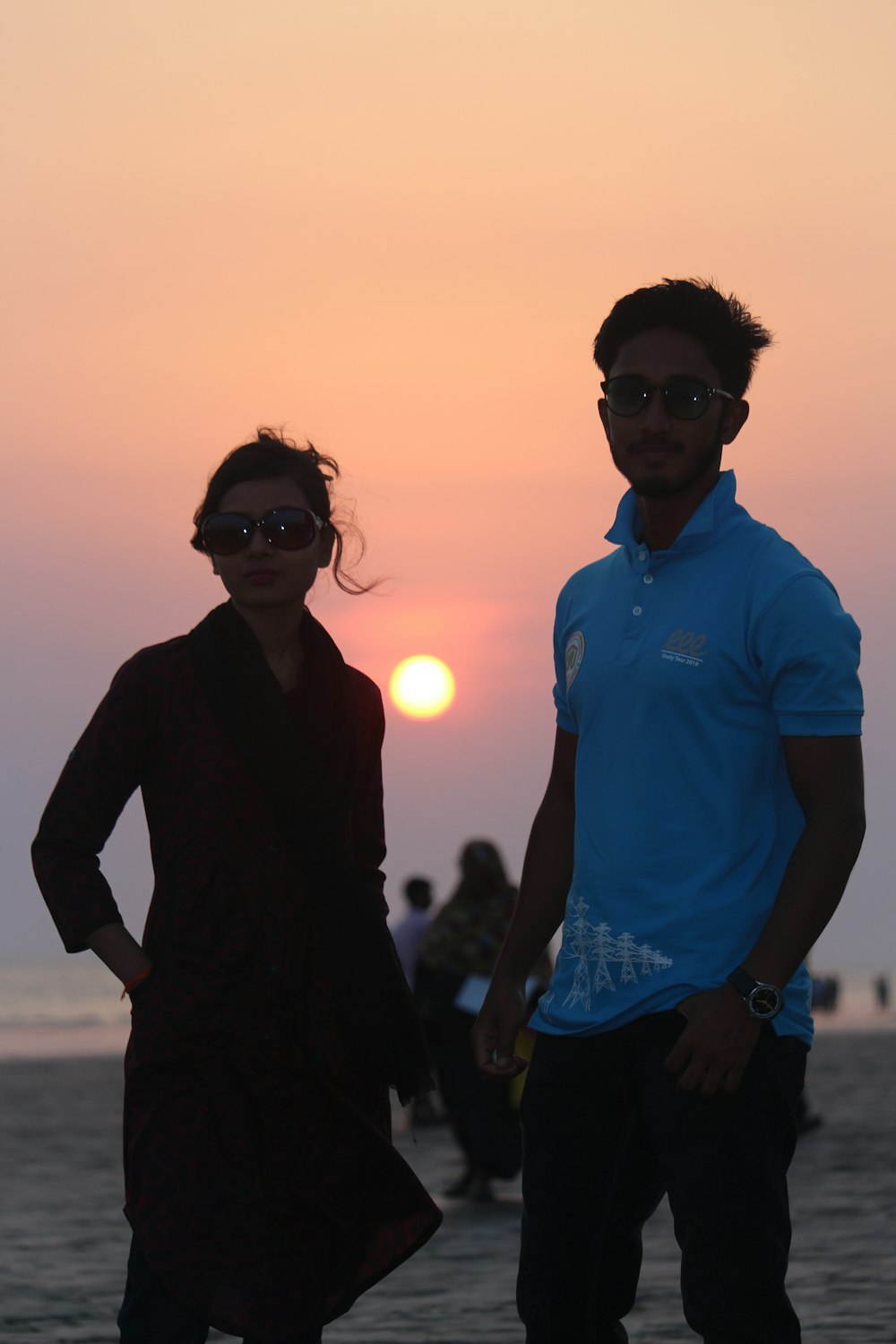 a man and a woman standing on a beach at sunset