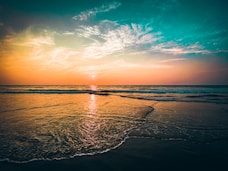 the sun is setting over the ocean on the beach