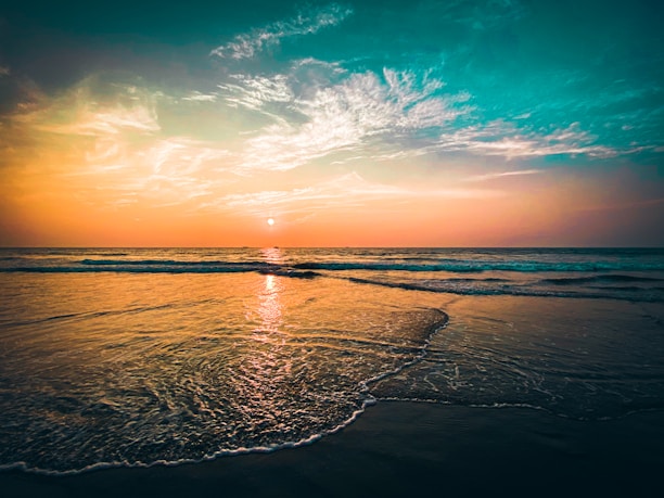the sun is setting over the ocean on the beach