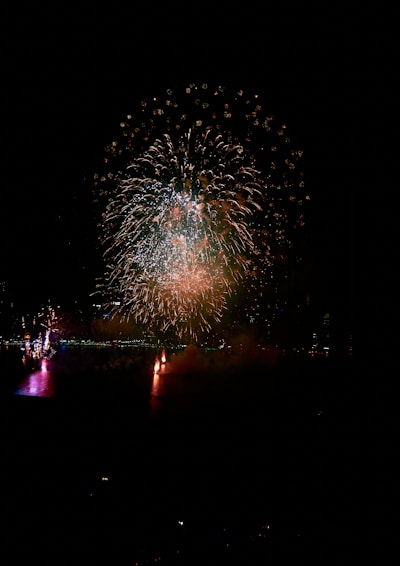 A vibrant nighttime fireworks display bursting over a scenic lake, reflecting colorful lights on the water.