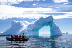 a group of people in a small boat in front of an iceberg