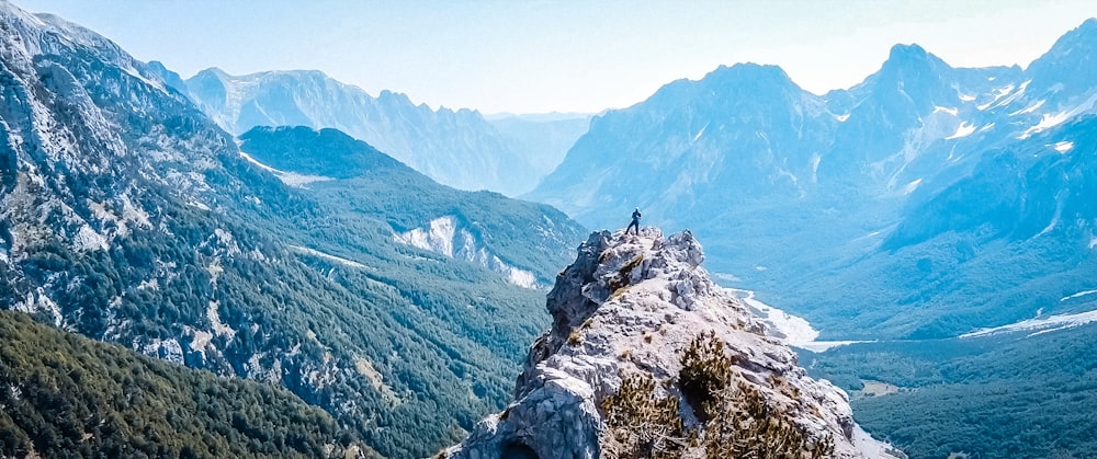 a man standing on top of a mountain next to a forest