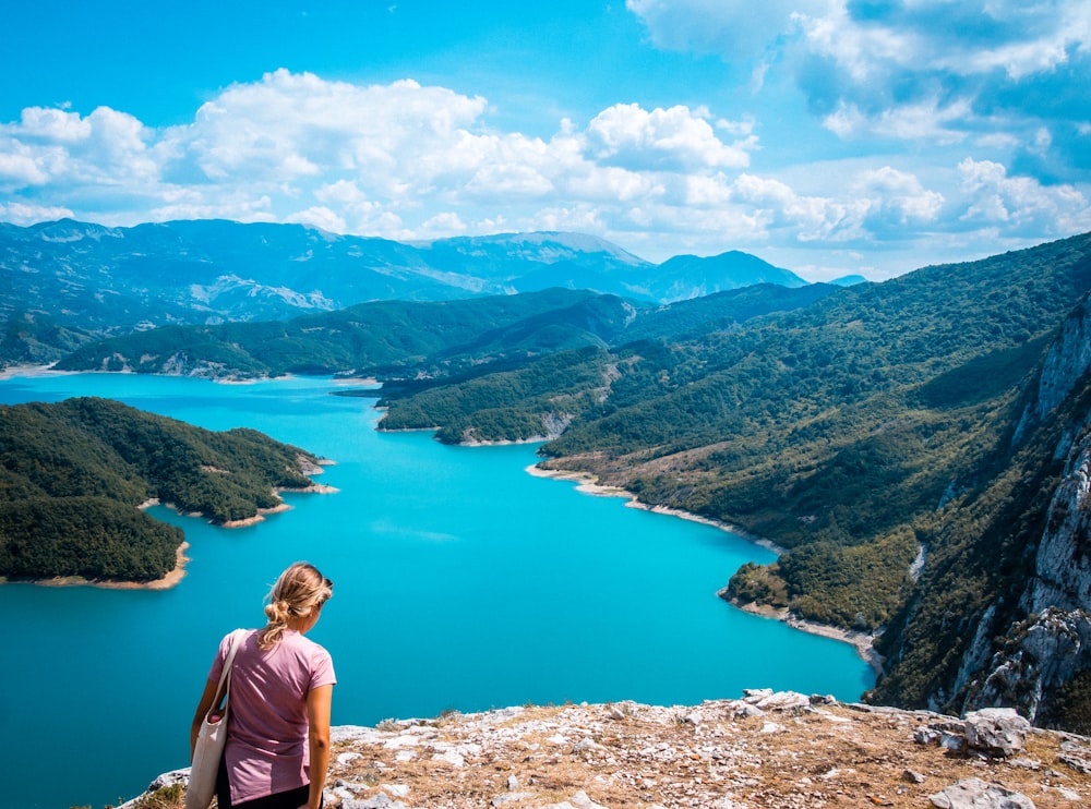 a woman standing on top of a mountain next to a lake