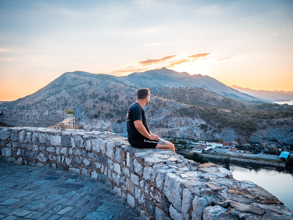 a man is sitting on a stone wall