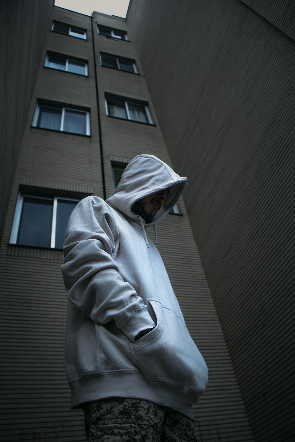 a man in a white hoodie standing in front of a tall building