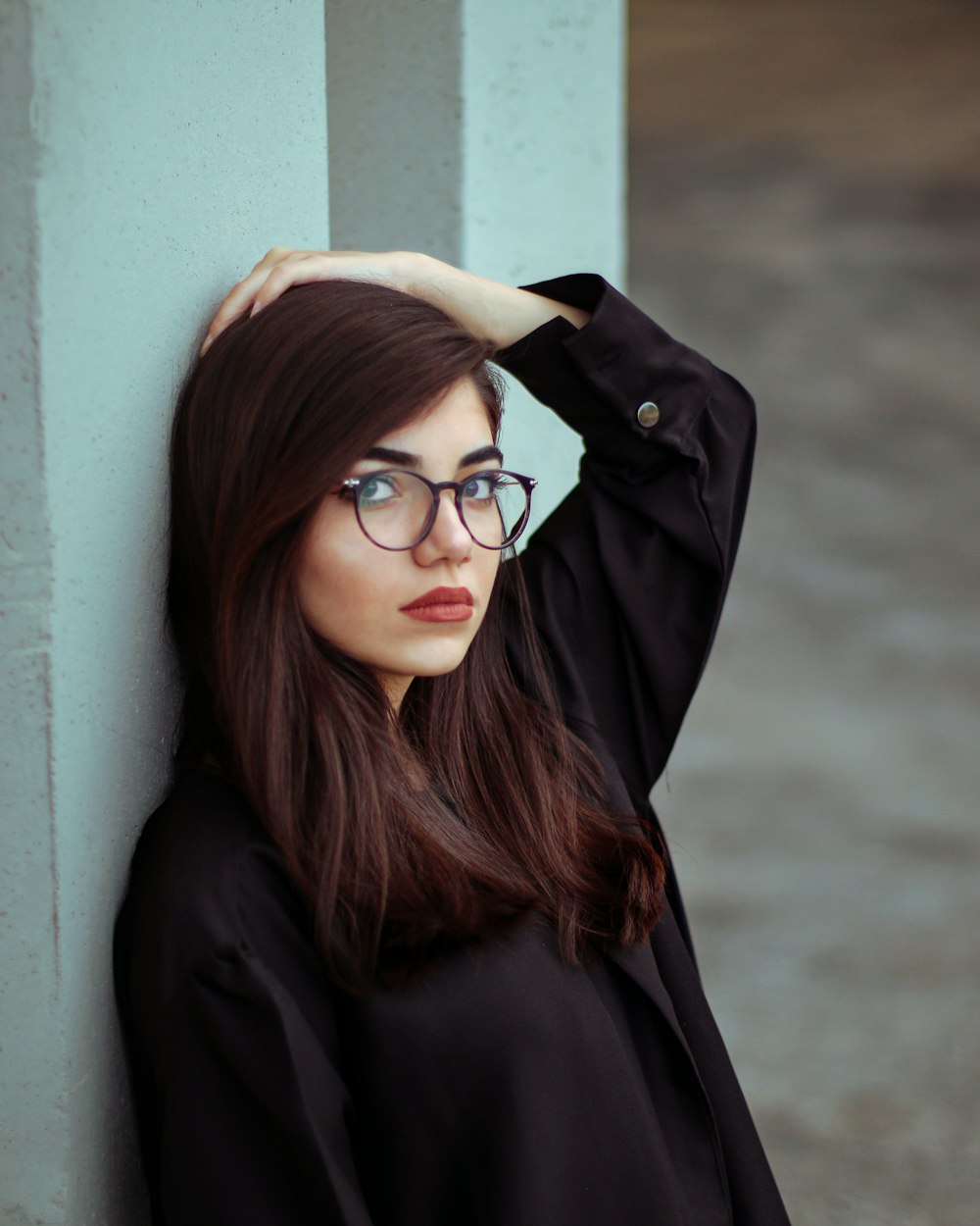 a woman wearing glasses leaning against a wall