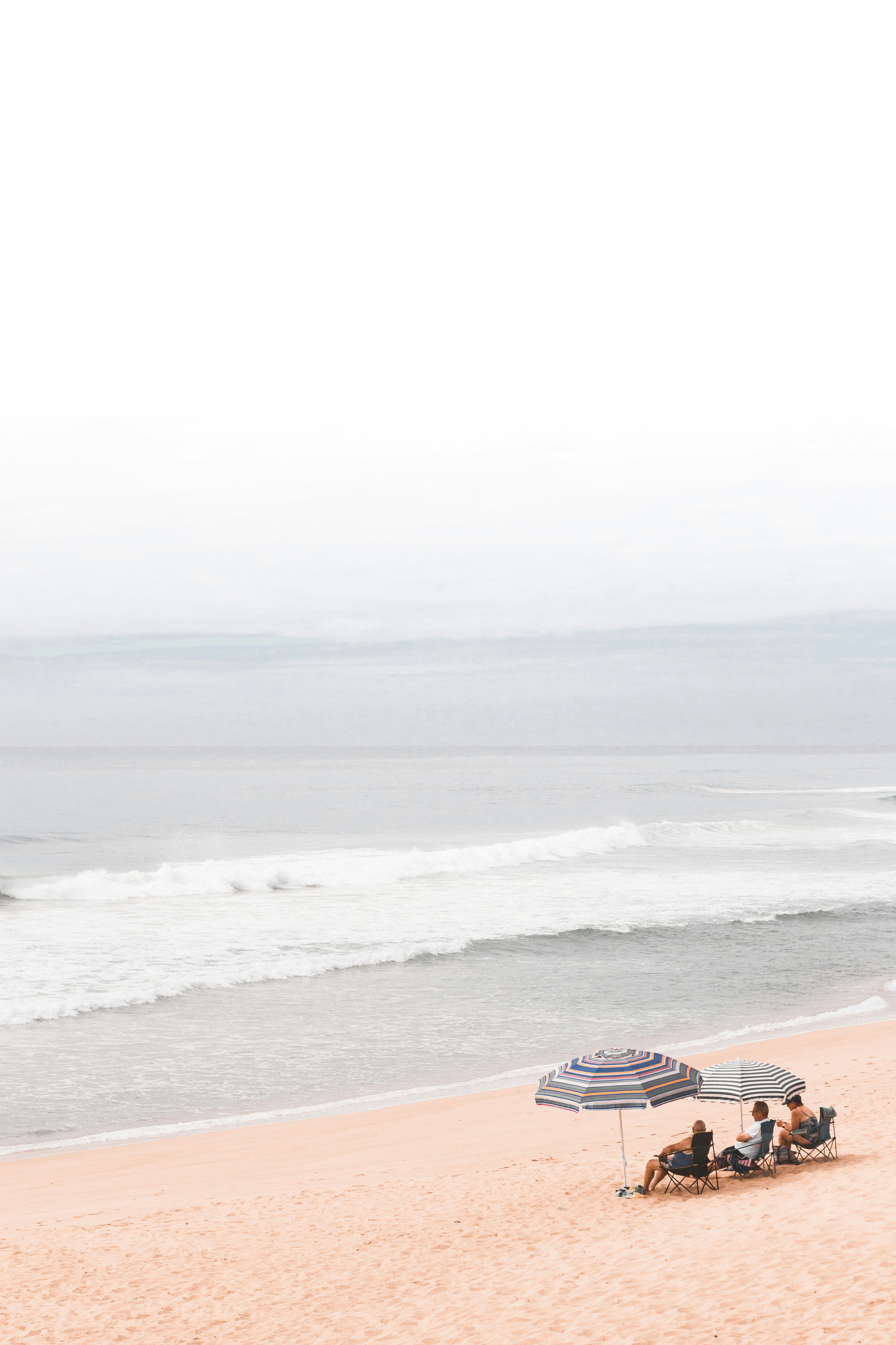 Three people sitting under umbrellas on the sand at Umdloti beach