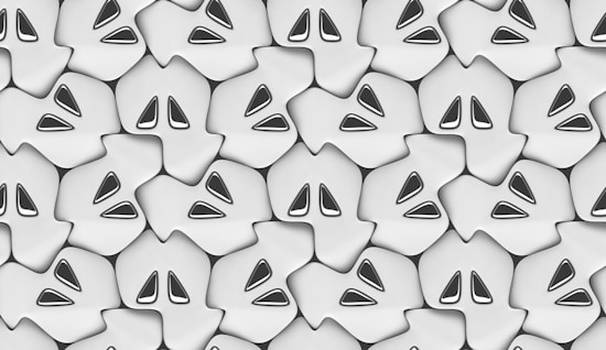 A seamless pattern of stylized ghost-like shapes with pointed features and hollow eyes, arranged closely together. The image has a monochromatic and abstract aesthetic.