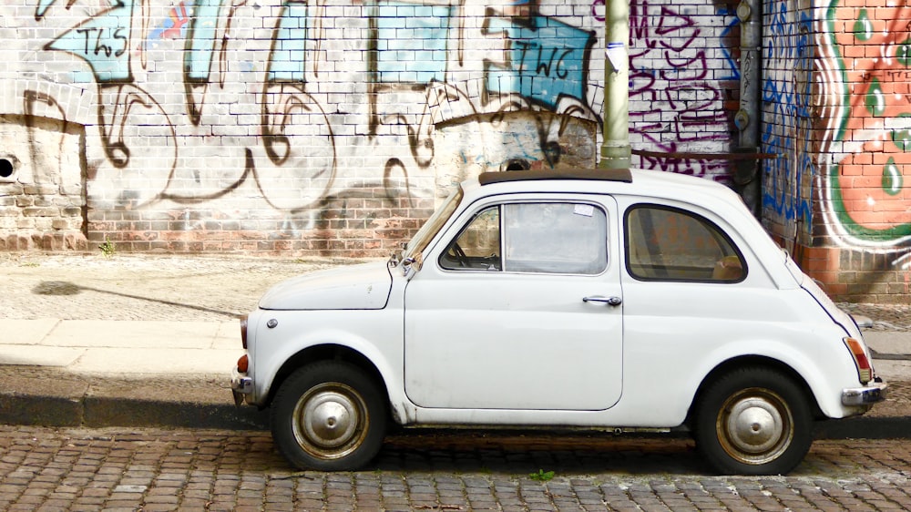 a small white car parked in front of a brick wall