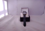 A sleek, modern watch with a polished metal band resting on a velvet cushion.