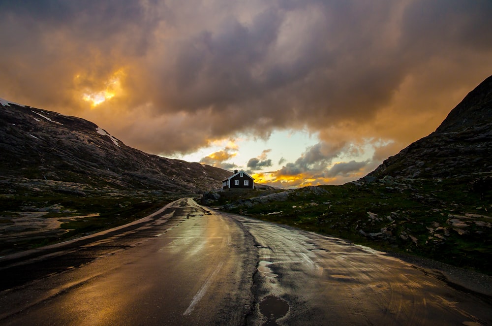 a road with a house in the distance under a cloudy sky