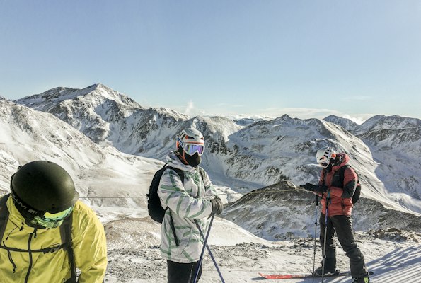 Three skiers standing on a snowy Pyrenean ridge with snow-covered peaks stretching into the distance