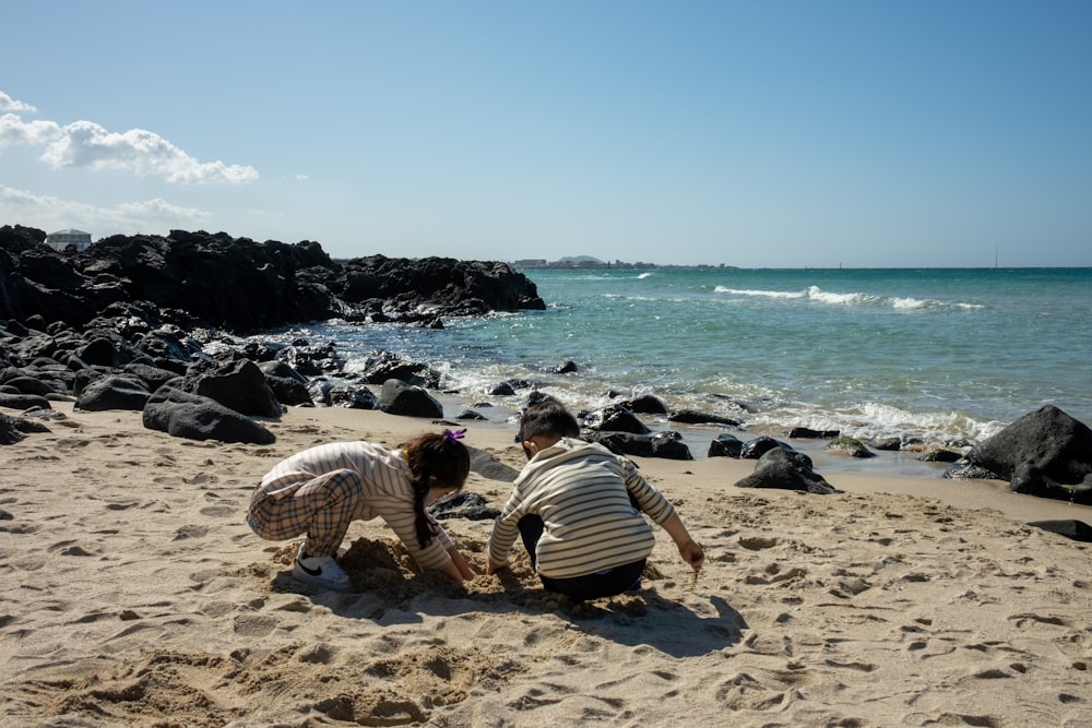 a couple of people sitting on top of a sandy beach