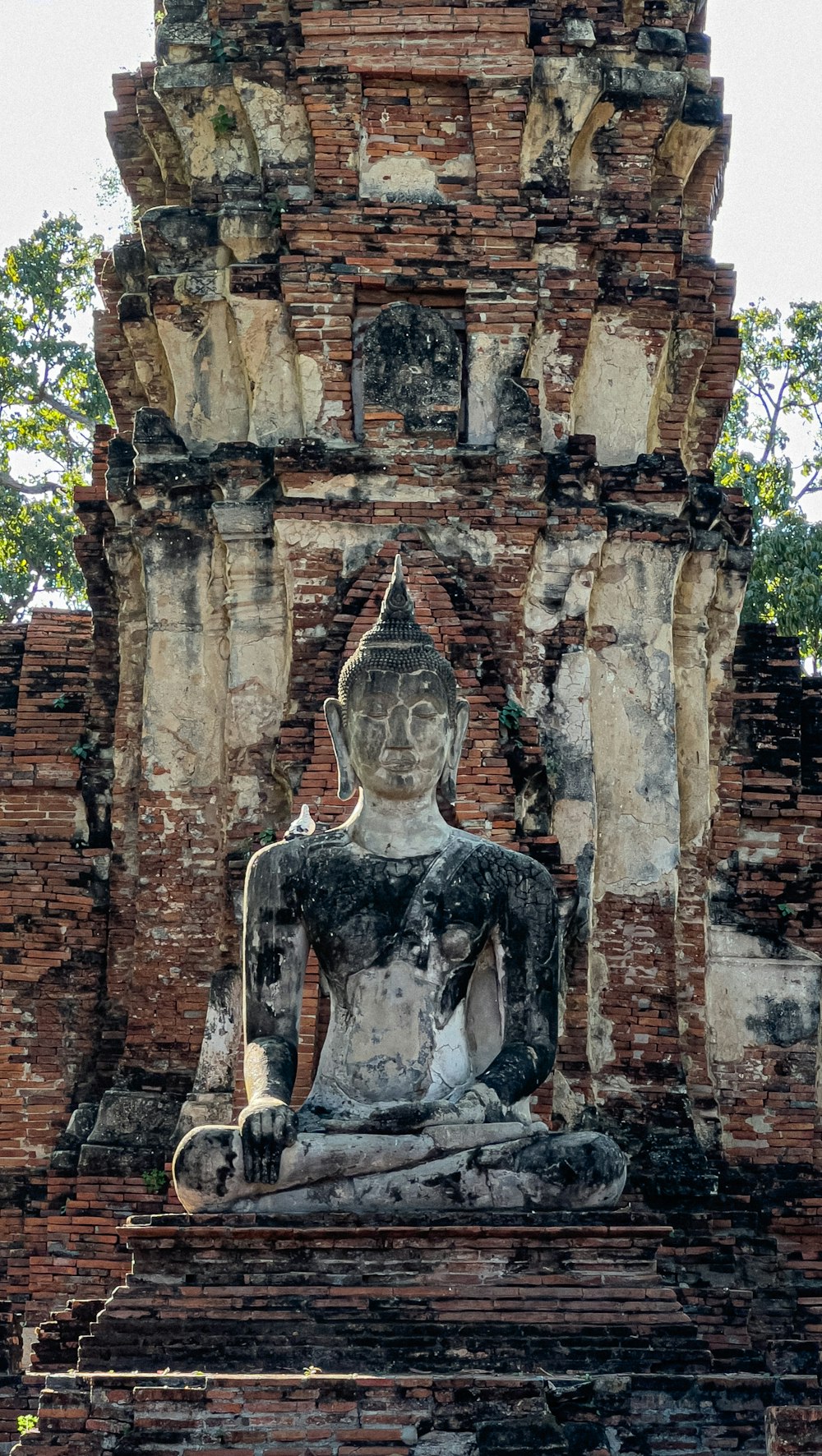 a statue of a buddha sitting in front of a brick wall
