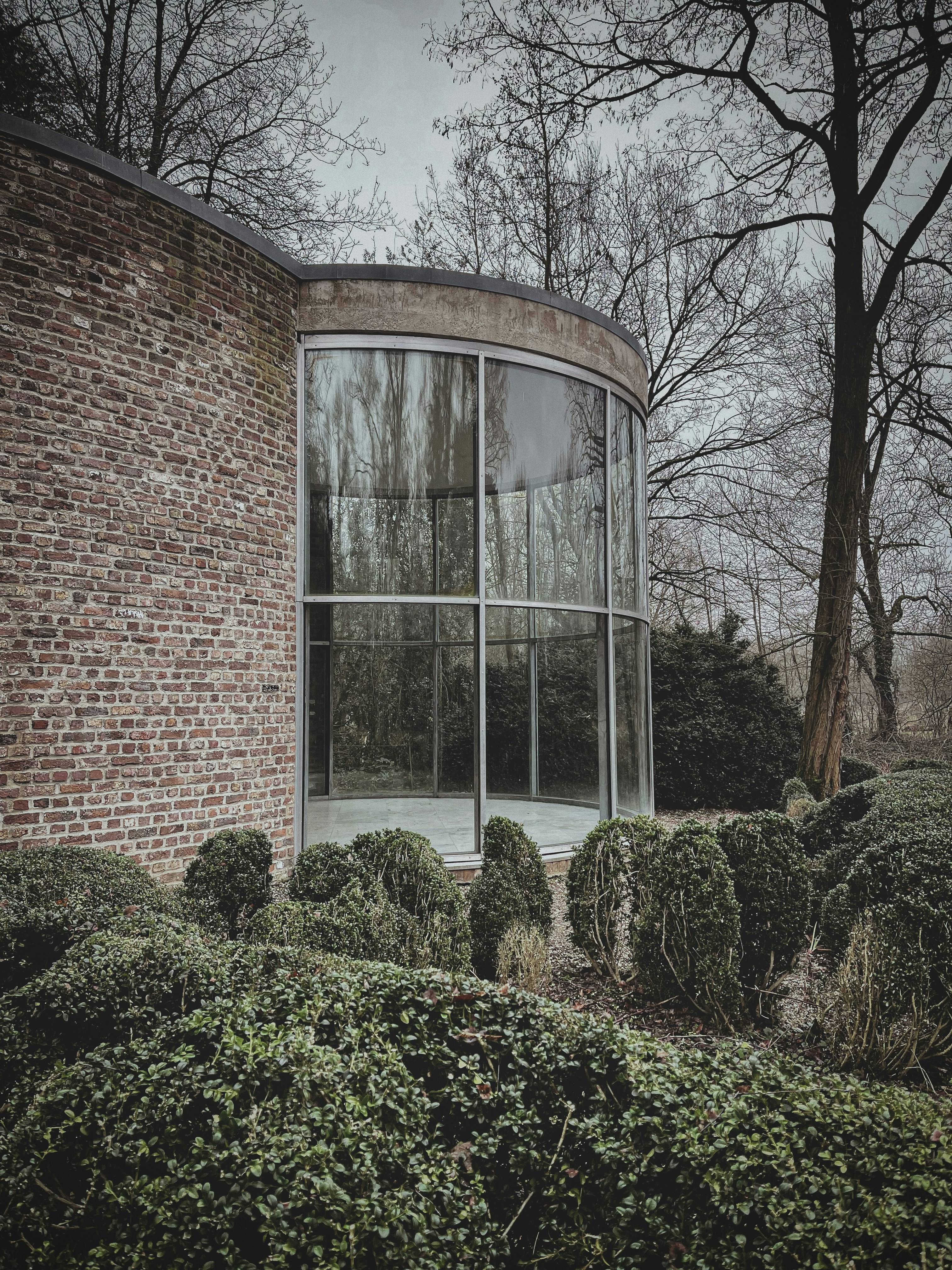 Ein rundes Fenster in einem Backsteingebäude, umgeben von Büschen