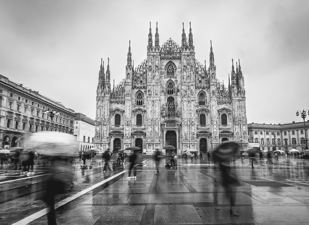 a black and white photo of people walking in front of a cathedral