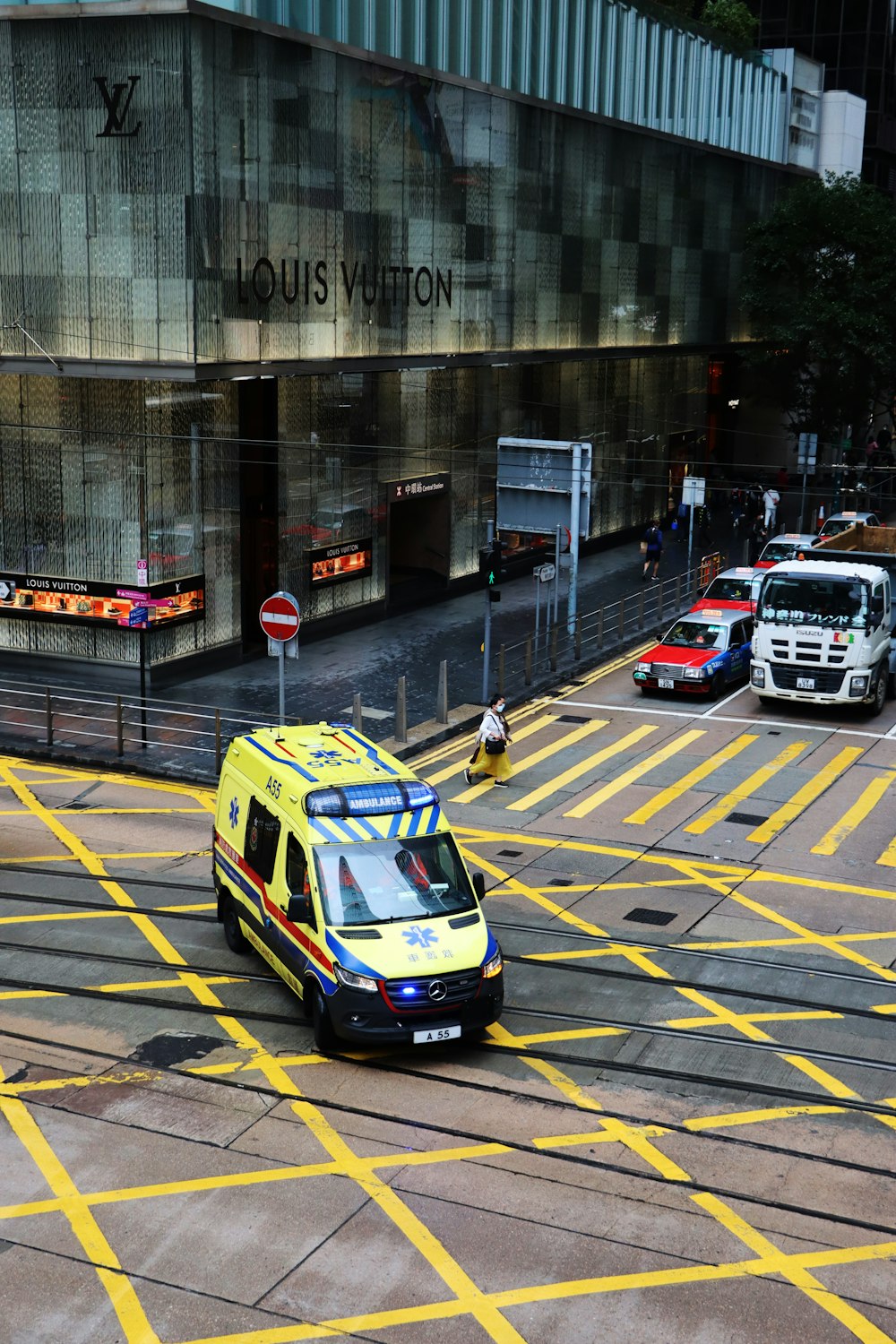 a yellow and blue ambulance driving down a street next to a tall building