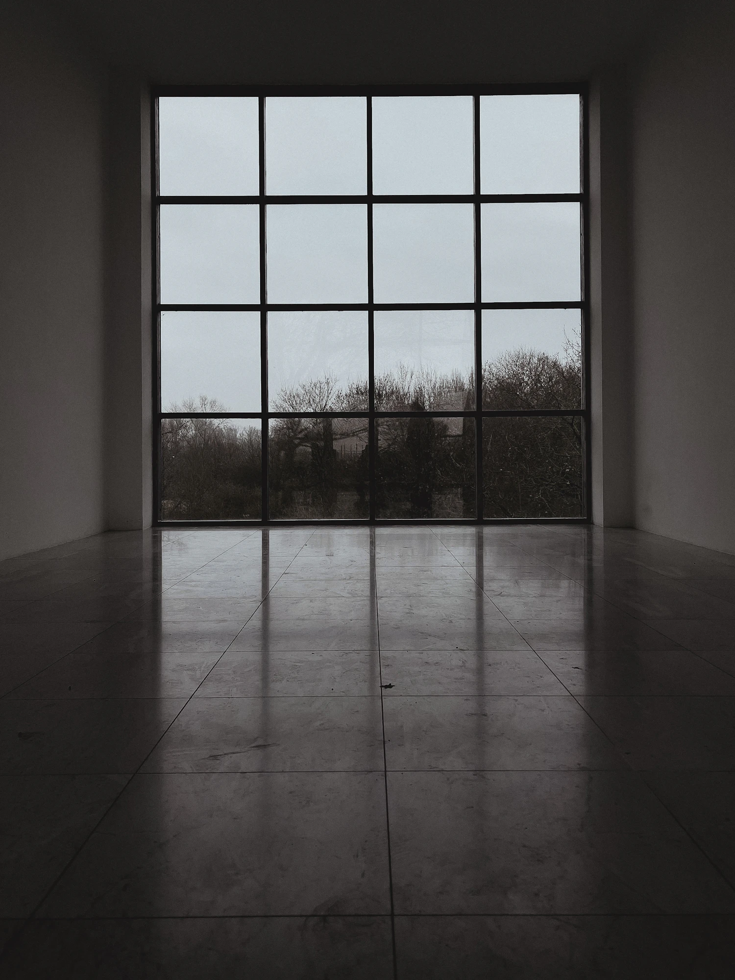 An empty room with a tall grid window at the far end and light lying flat across the floor