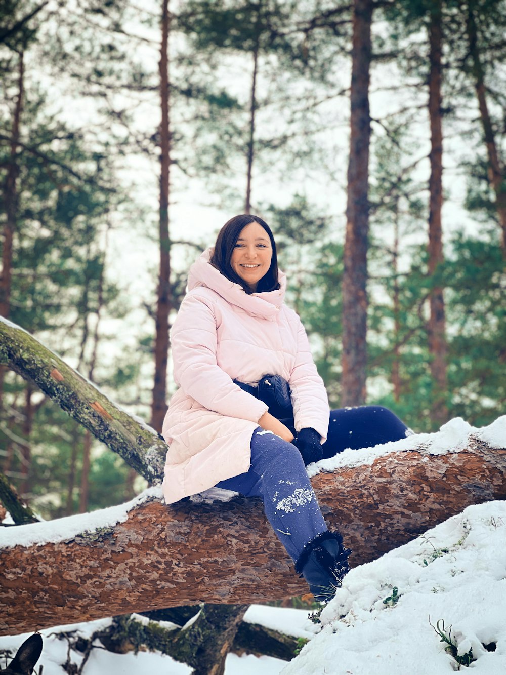 a woman sitting on a log in the snow